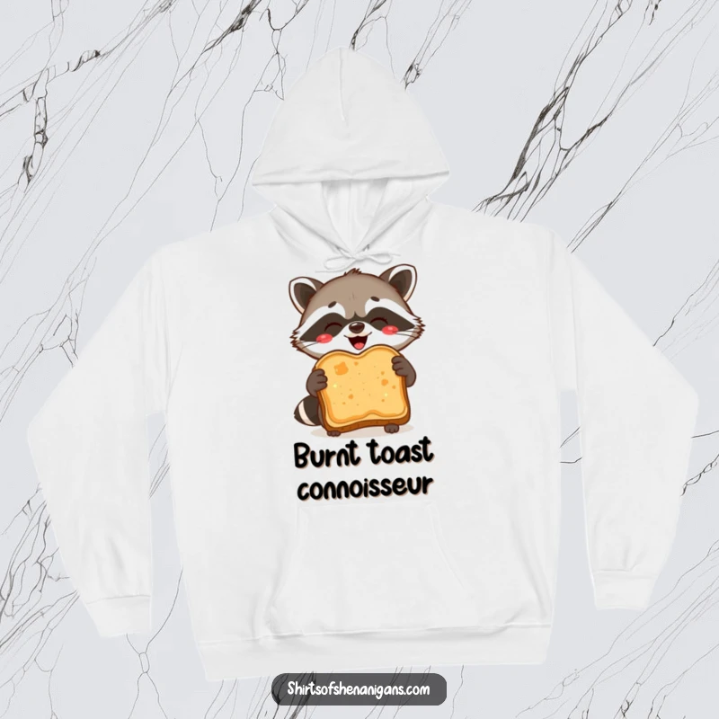 Funny Hoodie: A delighted raccoon proudly holds a burnt slice of toast, perfect for cozy humor.